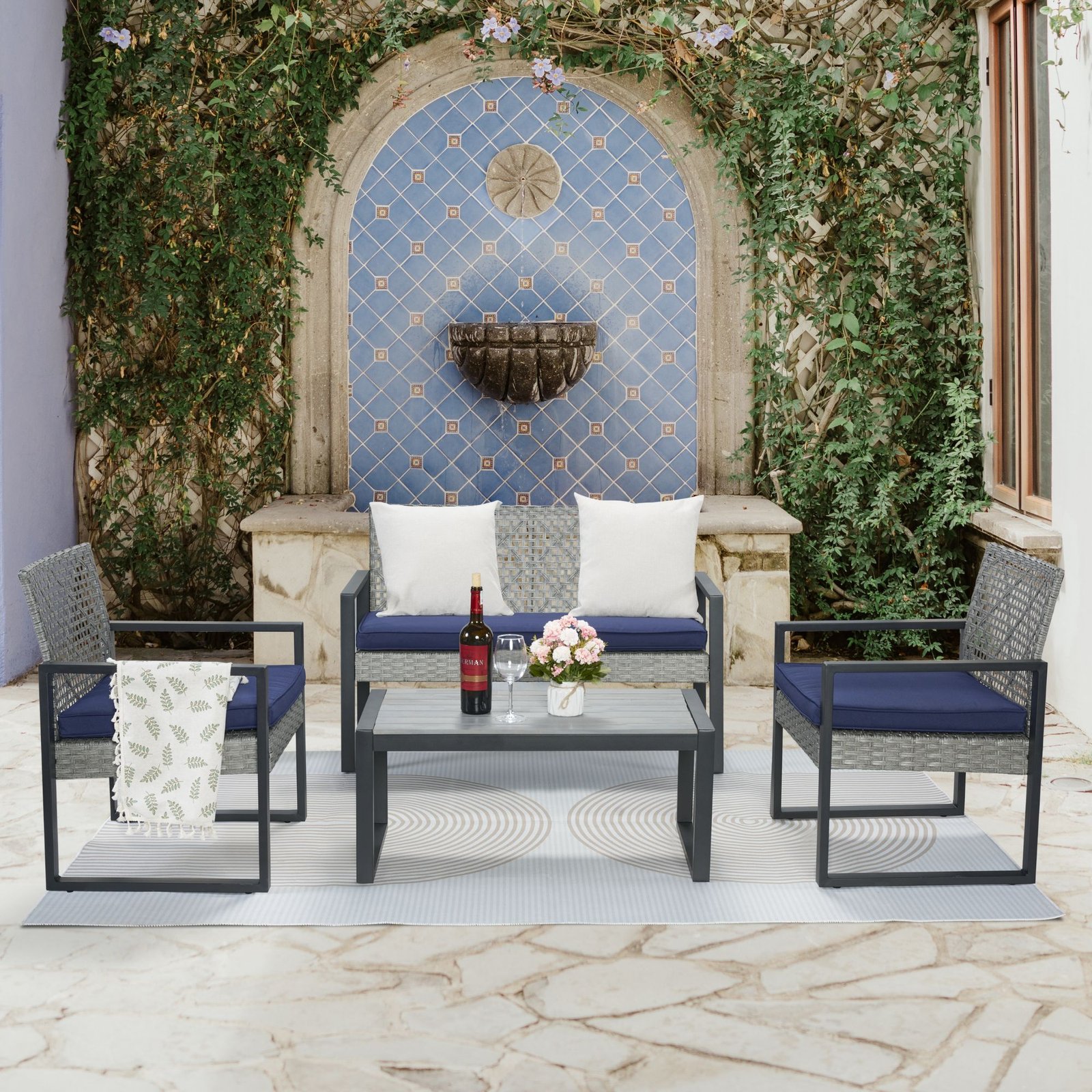 4-piece gray rattan patio sectional set arranged in courtyard with fountain and flowering greenery
