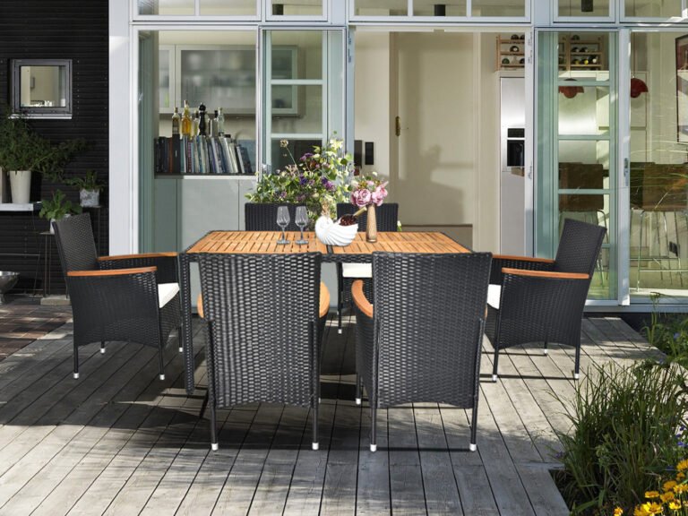 6-person rattan patio dining set on a backyard deck with glass doors, fresh flowers, wine glasses, and dinner plates