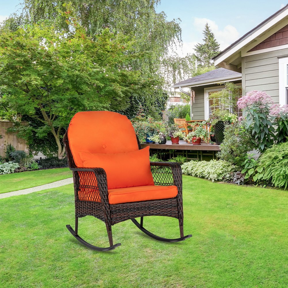 Brown outdoor wicker rocking chair placed in garden setting with lawn and potted plants