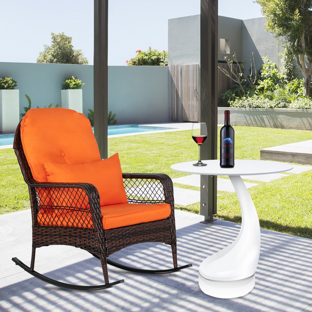 Brown outdoor wicker rocking chair on shaded patio with small side table and wine glass