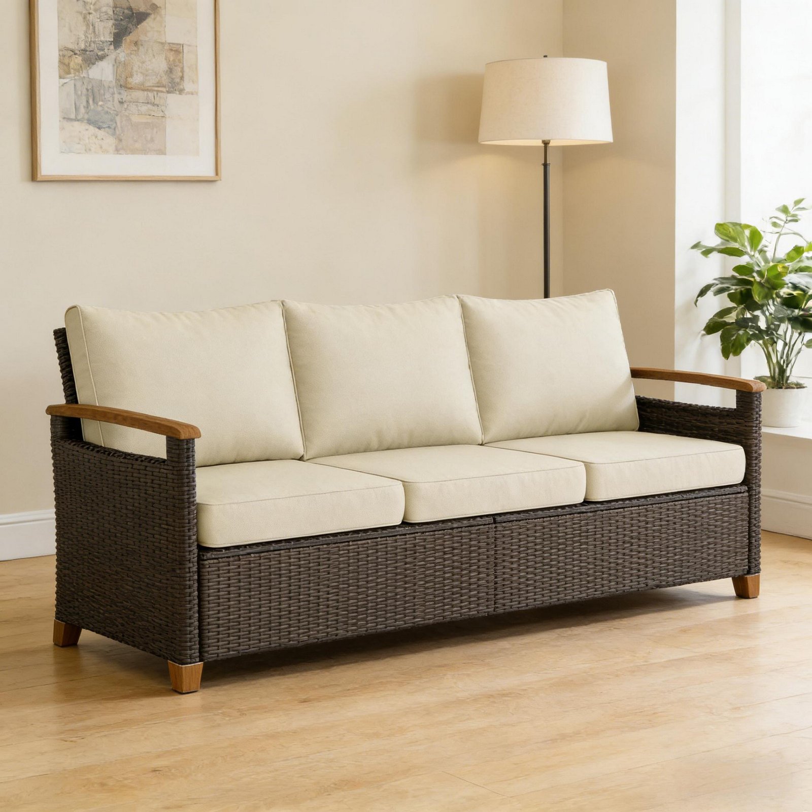 3-seater brown wicker patio sofa with beige cushions placed indoors near a window on wood flooring with floor lamp and plant