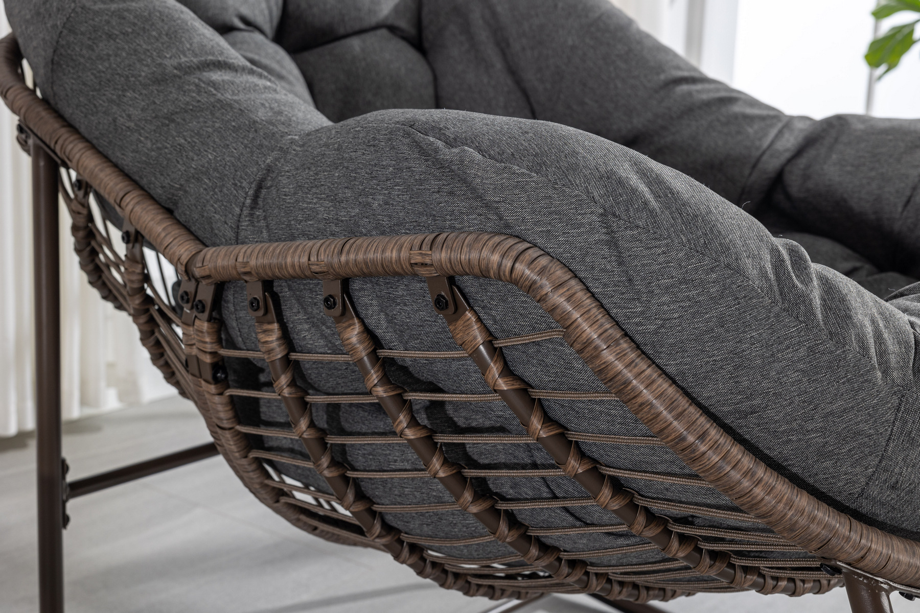 close-up of oversized outdoor rattan rocking chair showing wicker weave and cushion details