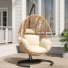 Heavy-duty U-base hanging egg chair in natural rattan with a cozy cushion, set against a green backyard garden patio background.