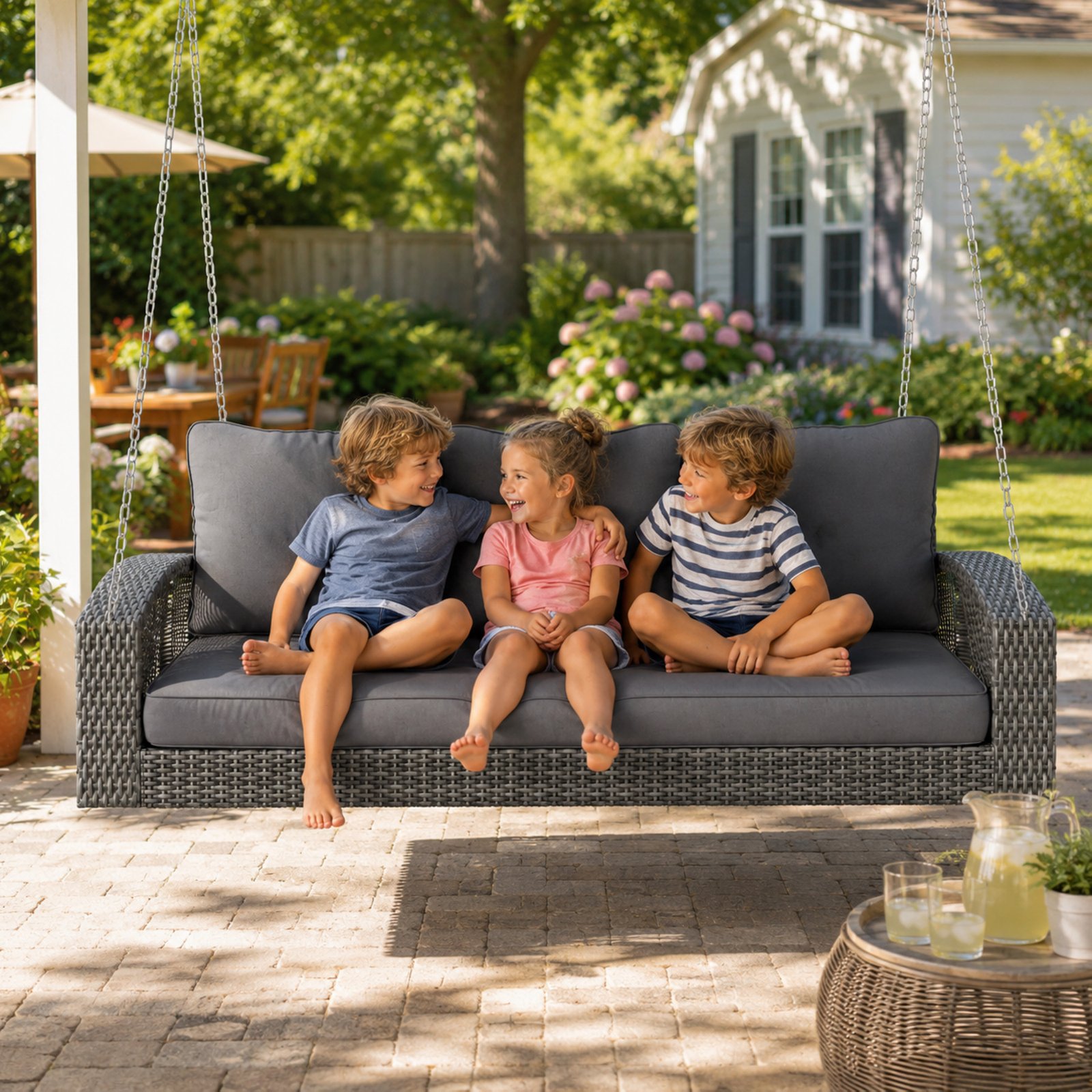 Three children sitting on a 69-inch 3-person wicker porch swing with gray cushions in a backyard patio setting.